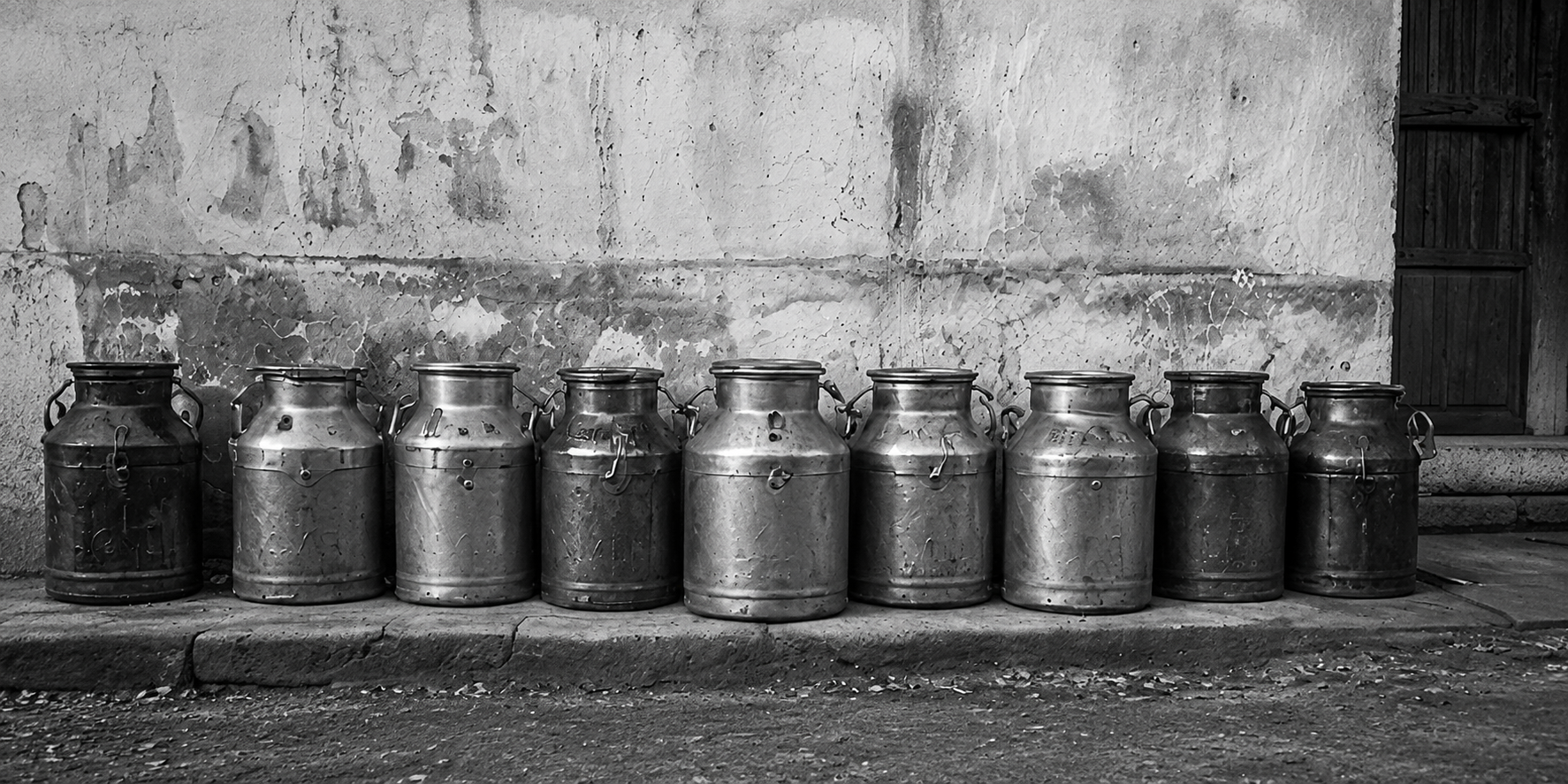 Traditional metal milk vessels arranged along a village wall